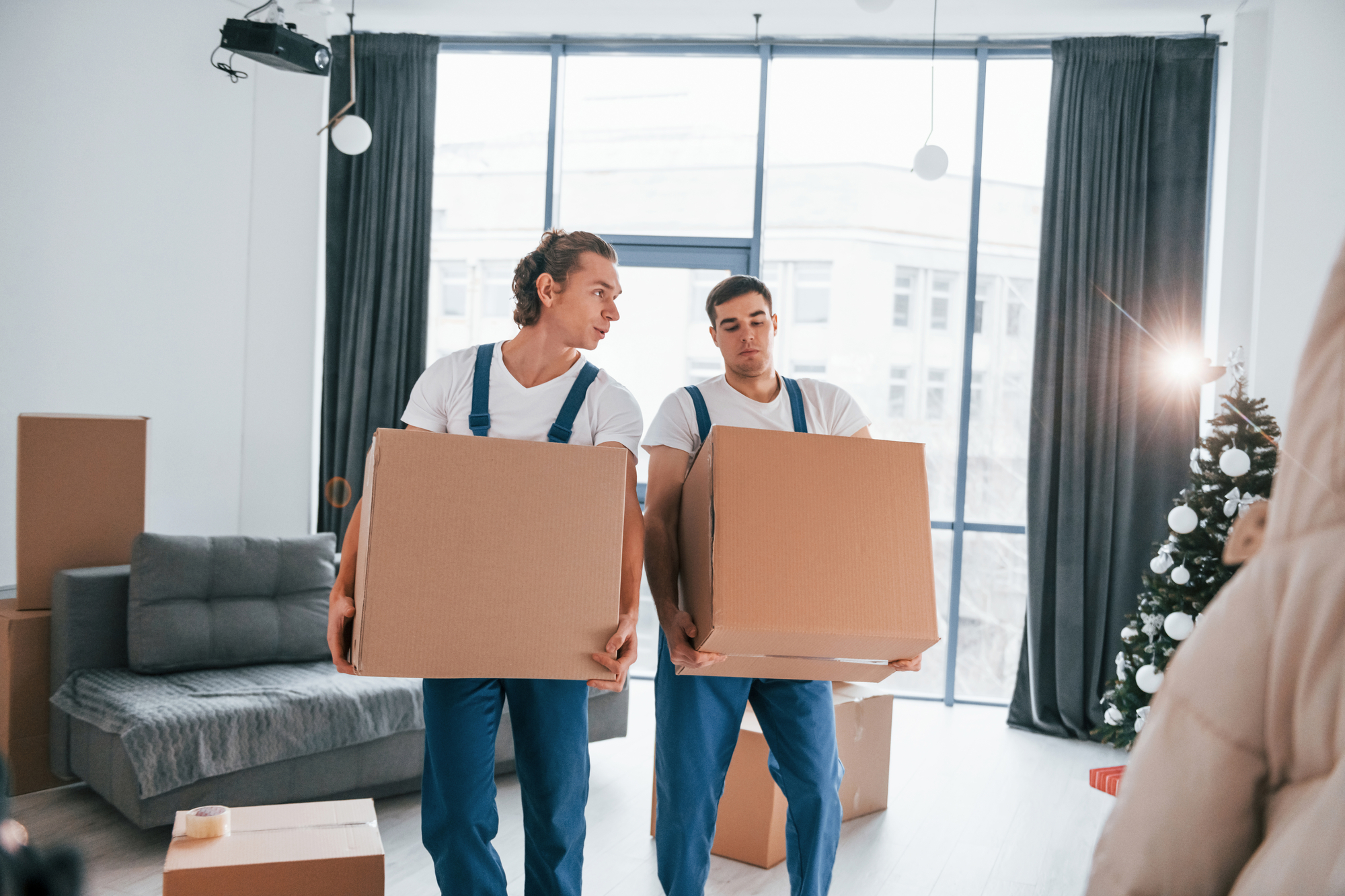 Two men transporting boxes in a spacious living room, preparing for a