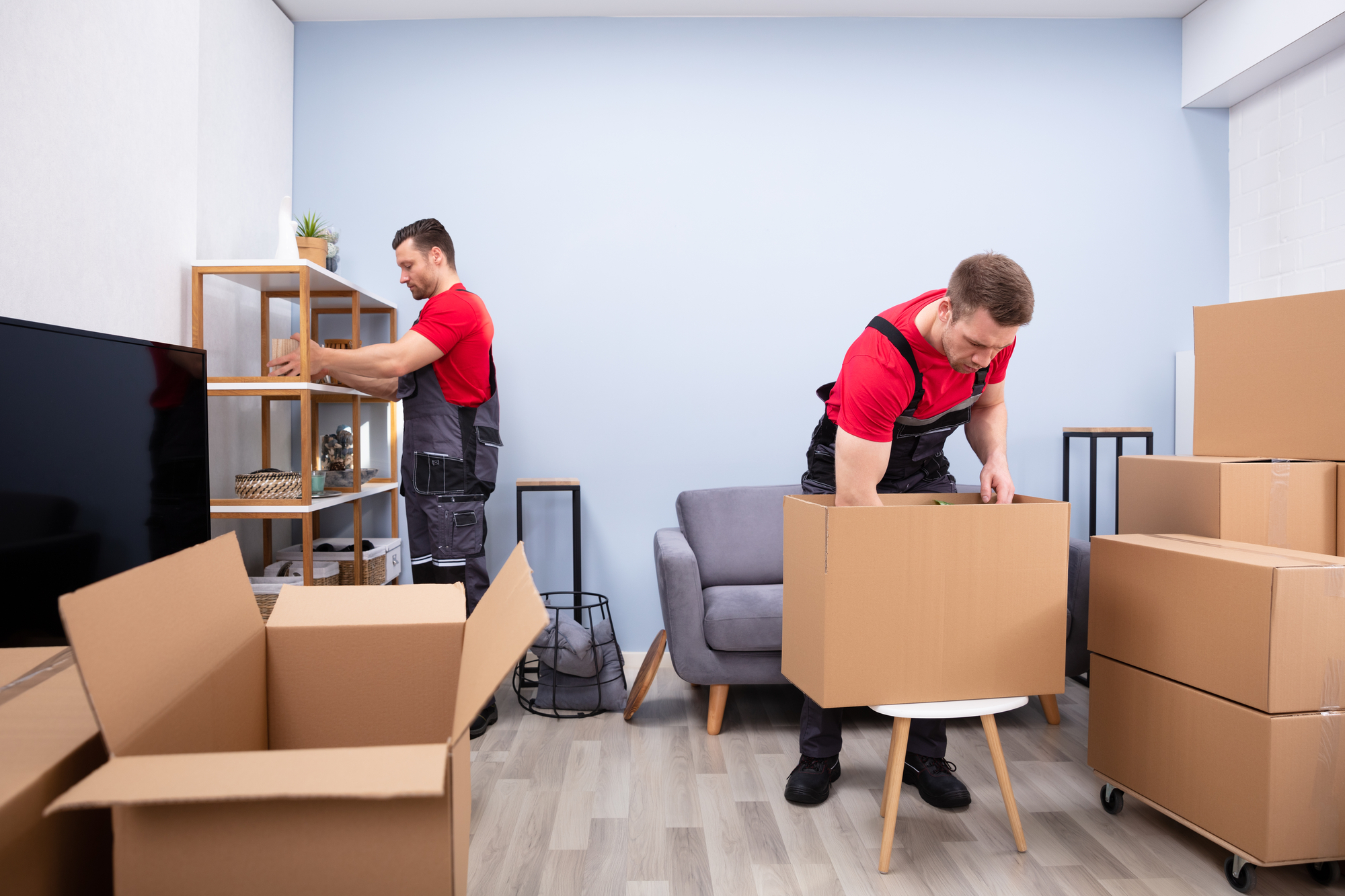 Two men are carefully moving boxes in a spacious office, preparing for