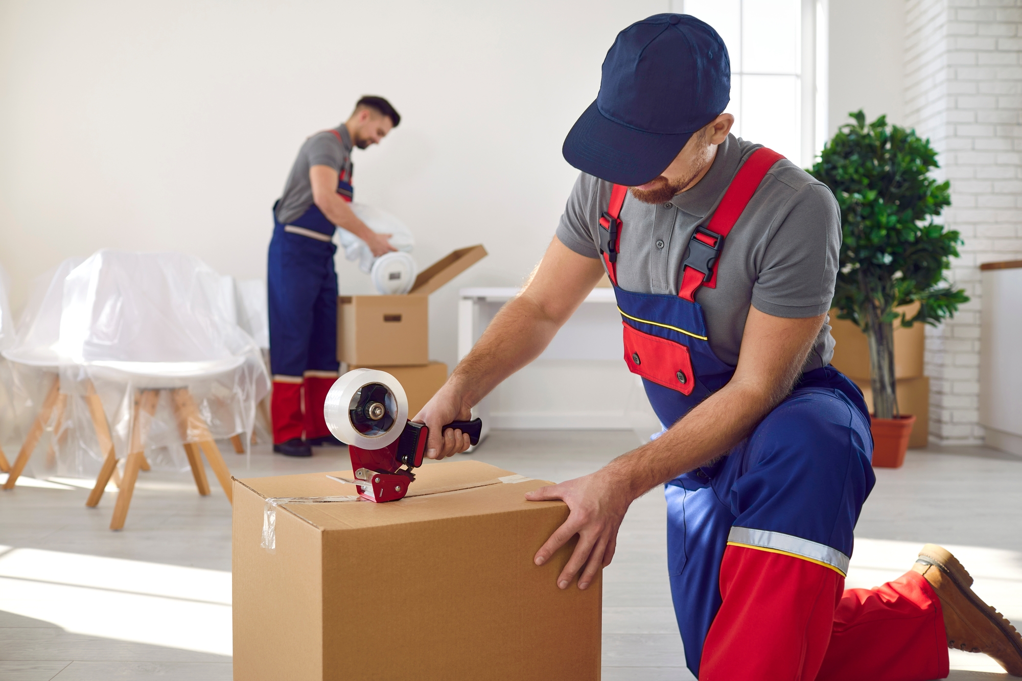 Two workers in overalls and hard hats are transporting boxes